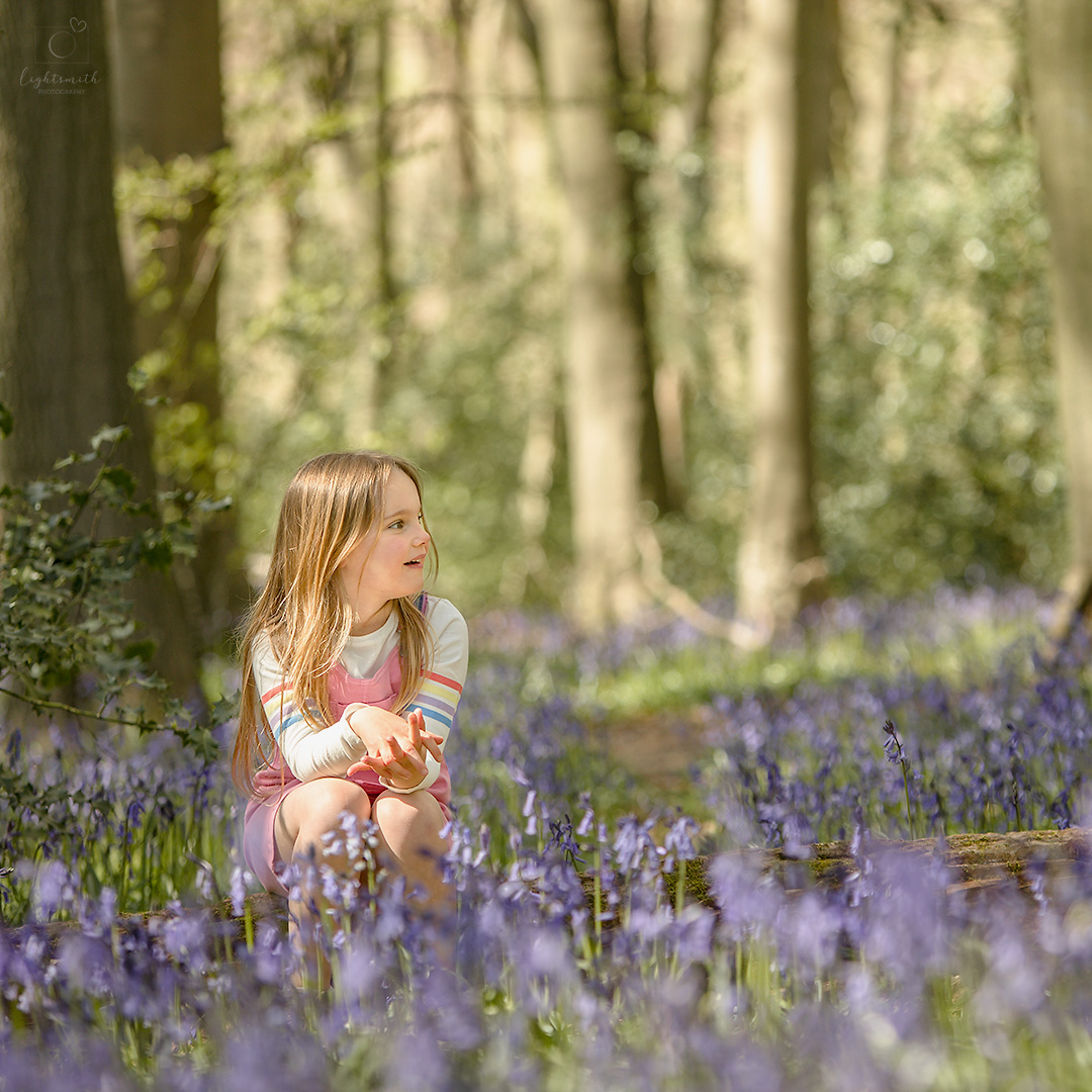 a little girl sits amongst the bluebells in a Buckinghamshire woodland. She is looking off to the right and smiling