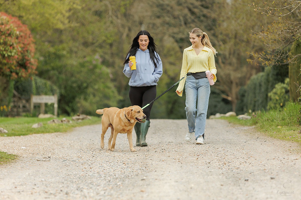 two women walking with a dog, having coffee. The dog is on a hands-free lead