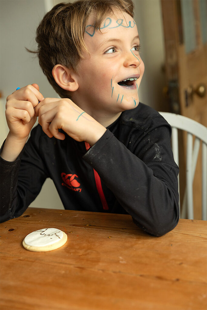 a boy crafting, he has drawn all over his face with blue marker pen and he is laughing